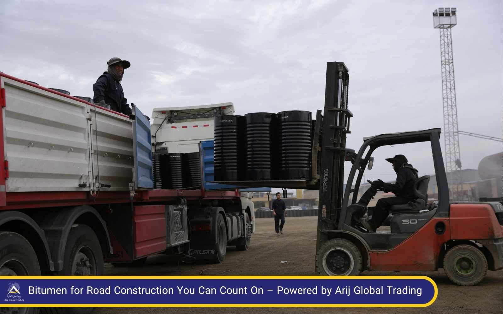 Efficient Bitumen Handling for Road Construction Projects – Arij Global Trading Forklift loading steel drums of bitumen for road construction onto a flatbed truck at Arij Global Trading's logistics yard