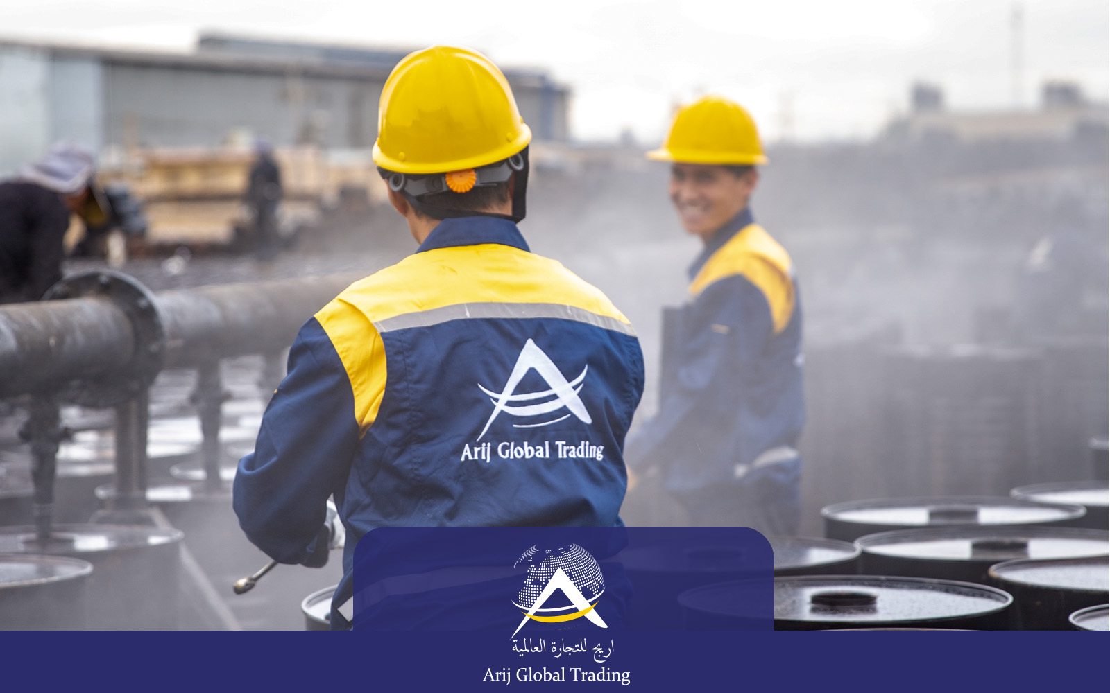 Two Arij Global Trading operational staff wearing branded blue and yellow uniforms and safety helmets overseeing the hot-filling process of export drums, with industrial steam visible on the active packaging line.