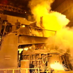 Steelmaking equipment surrounded by steam inside an industrial plant.