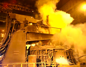 Steelmaking equipment surrounded by steam inside an industrial plant.